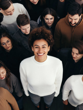 Capturing a high angle view of a joyful young woman smiling brightly while standing out in a diverse crowd, looking up at the camera with a sense of happiness and individualityの素材