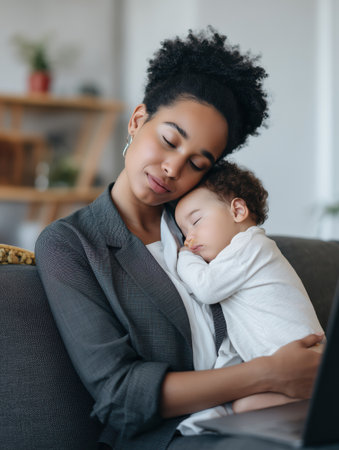 Tired african american mother wearing a blazer closing eyes while holding her sleeping baby on her lap, managing work life balance and remote professional duties from sofaの素材