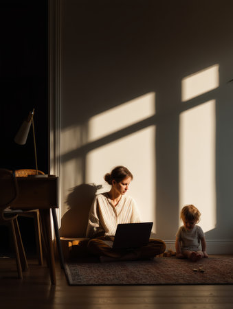 Mother managing remote work responsibilities while her toddler plays with wooden blocks on the rug, balancing modern family life and professional career at home during golden hourの素材