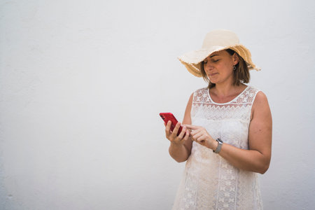 Woman using her phone and headphones with a hatの写真素材