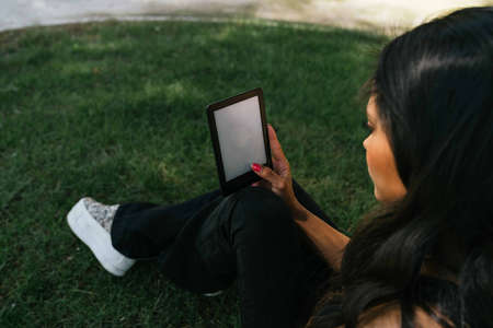 a girl reading an e-book on the lawnの写真素材