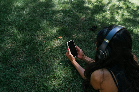 a Latin and brunette girl listening to music lying on the grass