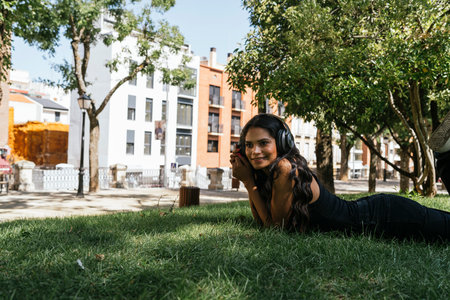 a Latin and brunette girl listening to music lying on the grassの写真素材