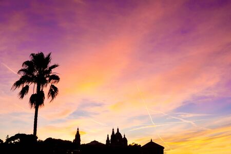Beautiful colorful sunset on Montjuic, Spain, black urban silhouette of a palm tree, churches, national art museum of catalonia, contrails and clouds.の写真素材