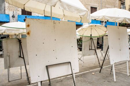 Empty dirty metal white easels on the street under white umbrellas. Street artists are gone for weekend. Selll paintings in the streets.の写真素材