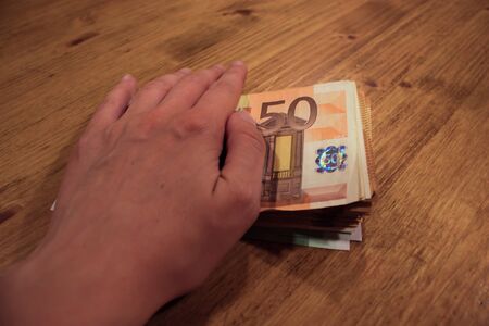 A female caucasian woman holding a hand of a stack of 50 euro banknotes. Bribes and taxes.の写真素材