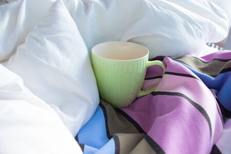 Green cup in bed with white blanket and striped duvet on a sunny dayの写真素材