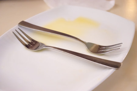 Orange juice on a white empty plate with two forks after eating a fruit salad