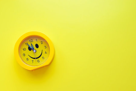 Yellow smiling round alarm clock on yellow background.