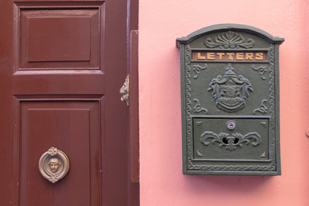 A bright retro looking green mailbox, or letterbox of a pink house. There's a brown door with gold...