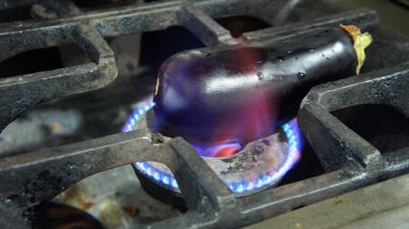 Fresh purple eggplant is grilled and burnt on the gas stove of a restaurant. Roasted aubergine recipe.の写真素材