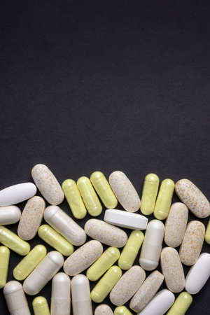 Pills, tablets, and capsules on black background, vertical flat lay. Painkillers, supplements, vitamins and antibioticsの写真素材