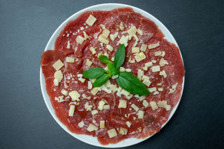 Marbled beef carpaccio with basil and parmesan cheese. Black background. Top view.の写真素材