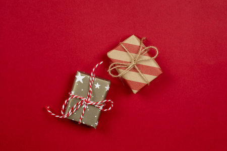 Two wrapped christmas presents and gift boxes wrapped in craft paper top view on red background with stripes and stars and copy space.の写真素材