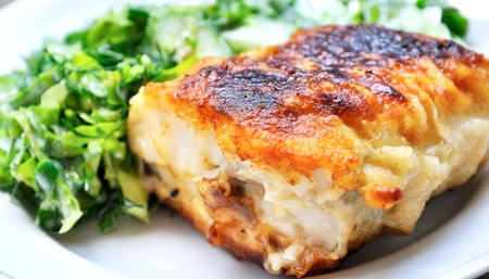 Piece of well-done fish with greens on a plateの写真素材