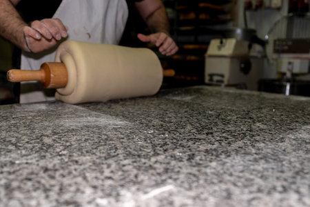 baker rolls the croissant dough on the rolling pin to stretch it again and mix the ingredients well in a bakeryの写真素材