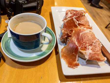 Beautiful image of the best Spanish breakfast, a toast of soft and crunchy homemade bread with grated tomato and a good serrano ham on top accompanied with a coffee with milkの写真素材