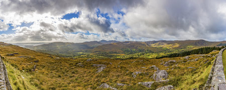 Panorama picture of typical Irish landscape with green meadows and rough mountains during daytimeの写真素材