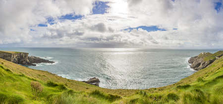 Panorama picture of typical Irish coast line with green meadows and blue waters during daytimeの写真素材