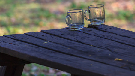 Picture of empty drinking glasses standing at the edge of a rustic wooden table at the risk of...