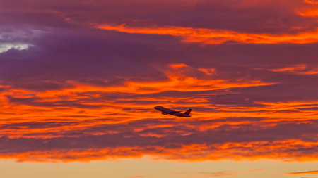 Footage of a plane in flight in front of low red ornage glowing clouds in the evening red