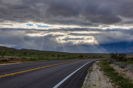 Picture of an empty road in the desert of california with cloudy sky with isolated sunbeams during...