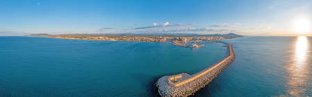 Drone panorama of the Spanish town of Vinaros with the large breakwater at the entrance to the port during sunrise in summerの写真素材