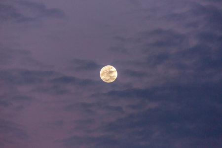Image of full moon against colorful evening sky with light clouds in summer