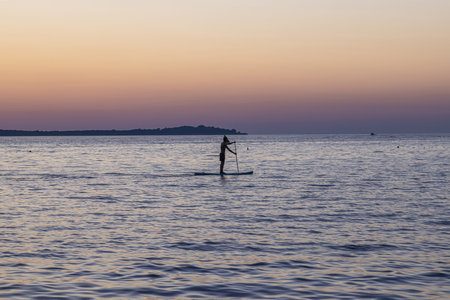 Picture of a single standup paddler in the evening in front of the setting sun in summer