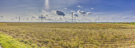 Panoramic image of a wind farm with a coal-fired power plant in the background during the day