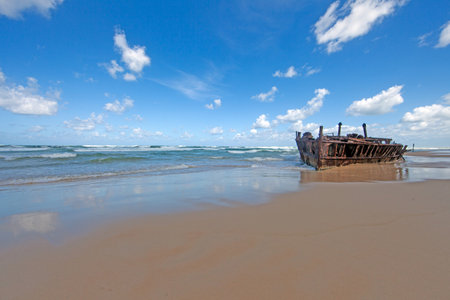 Shipwreck on Fraser Island with waves, sandy beach, and vibrant blue sky during daytimeの写真素材
