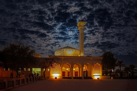 Illuminated mosque under dramatic cloudy night sky with glowing full moon in summerの写真素材