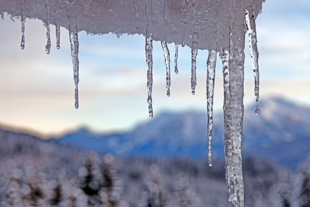Close up of icicles with blurred mountain landscape in winter during daytime