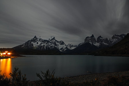 Night view of Lake Pehoe with Torres del Paine mountains and a lit lodge under dramatic cloudy skies in 2015の写真素材