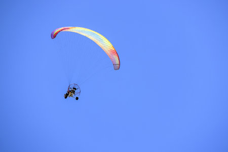 Paramotor glider with colorful parachute flying through a bright blue sky at Benotoa Beachの写真素材