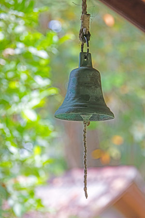 Close up of a hanging bronze temple bell surrounded by tropical greenery with no people visible in daylightの写真素材