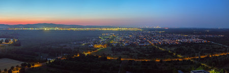 Wide aerial view over Frankfurt Airport and skyline at dusk with lights and distant mountainsの写真素材