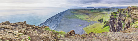 Wide panoramic view of black sand beach near Reynisfjara Iceland with dramatic coastline