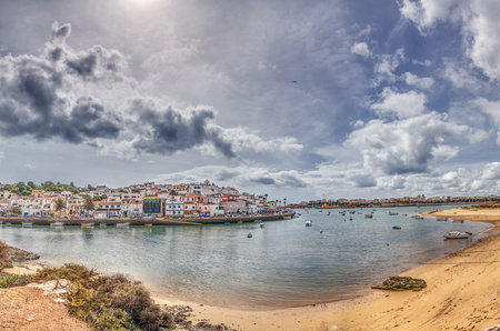 Panoramic view of Ferragudo with boats on the Arade River facing Portimao Algarve Portugal under cloudy sky.の写真素材