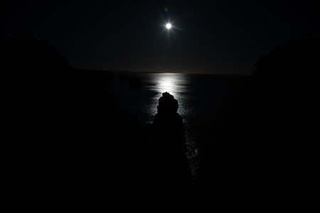 Night scene with bright moon reflection on calm ocean and dark sea cliffs in Algarve Portugalの写真素材
