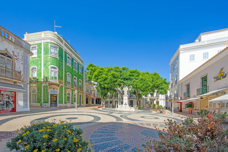 Colorful mosaic square with green tiled house trees and cafes in Loule Algarve Portugal under a clear blue skyの写真素材