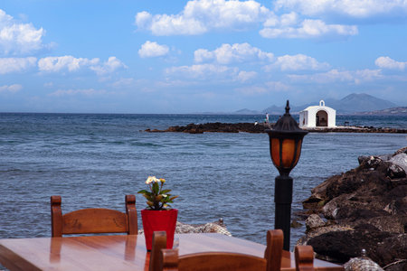 White coastal chapel on rocky shore of Georgioupolis Crete with blue sky and calm sea no peopleの写真素材