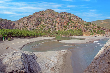 Scenic river flowing into sea at Preveli Beach Crete surrounded by mountains and treesの写真素材