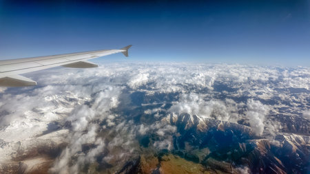 Aerial view of the Central Alps with snow capped mountains and airplane wing under bright blue sky