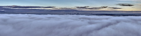 Aerial drone view of skyline emerging above rising ground fog during a colorful evening atmosphereの写真素材