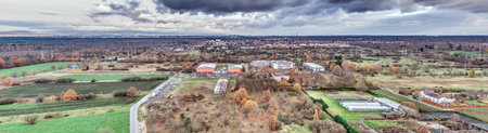 Wide aerial view of Moerfelden-Walldorf showing forest, fields, residential areas and the distant Frankfurt skyline under a cloudy sky.の写真素材