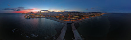 Drone panorama of Barcelona at blue hour with illuminated skyline beach and marina. City lights reflect on Mediterranean sea creating vibrant urban travel scene.の写真素材