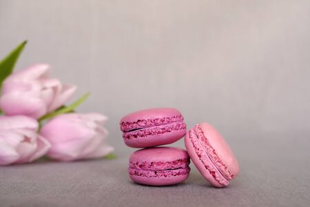 Stack of delicious colorful pink and purple macaron cookies on grey background with flowers. Space for text. French pastry and confectionery.の写真素材