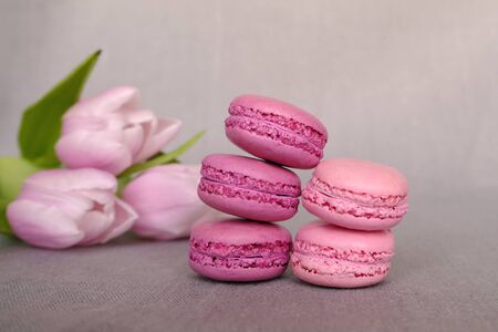 Stack of delicious colorful pink and purple macaron cookies on grey background with flowers. Copy space. French pastryの写真素材