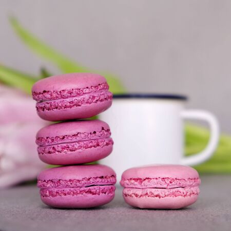 Close up of sweet french macarons, cup of tea or coffee and spring flowers on grey background. Colorful sandwich cookiesの写真素材